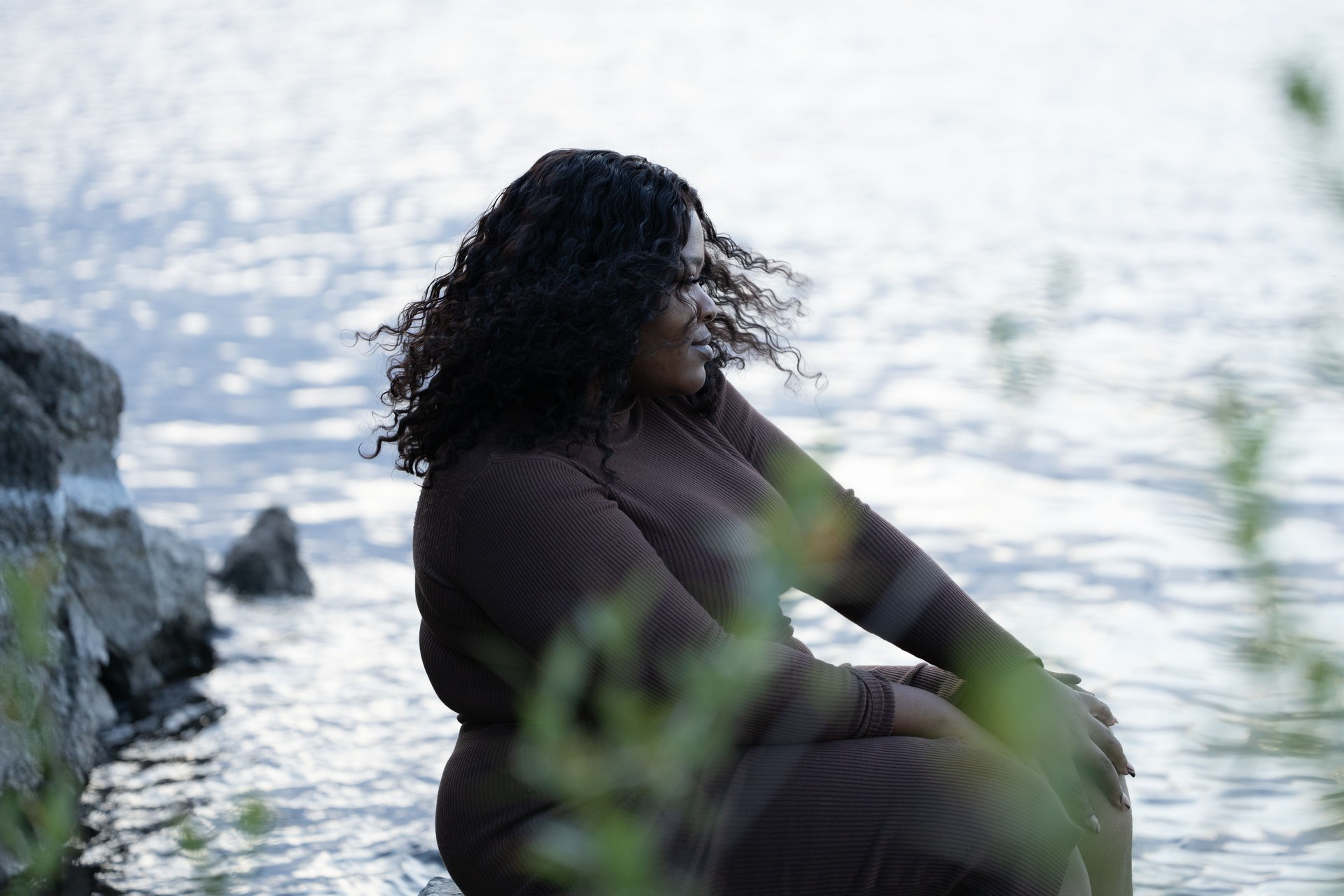Pretty curly black plump African American interracial woman sitting by the sea or river coast, shaking hair in summer