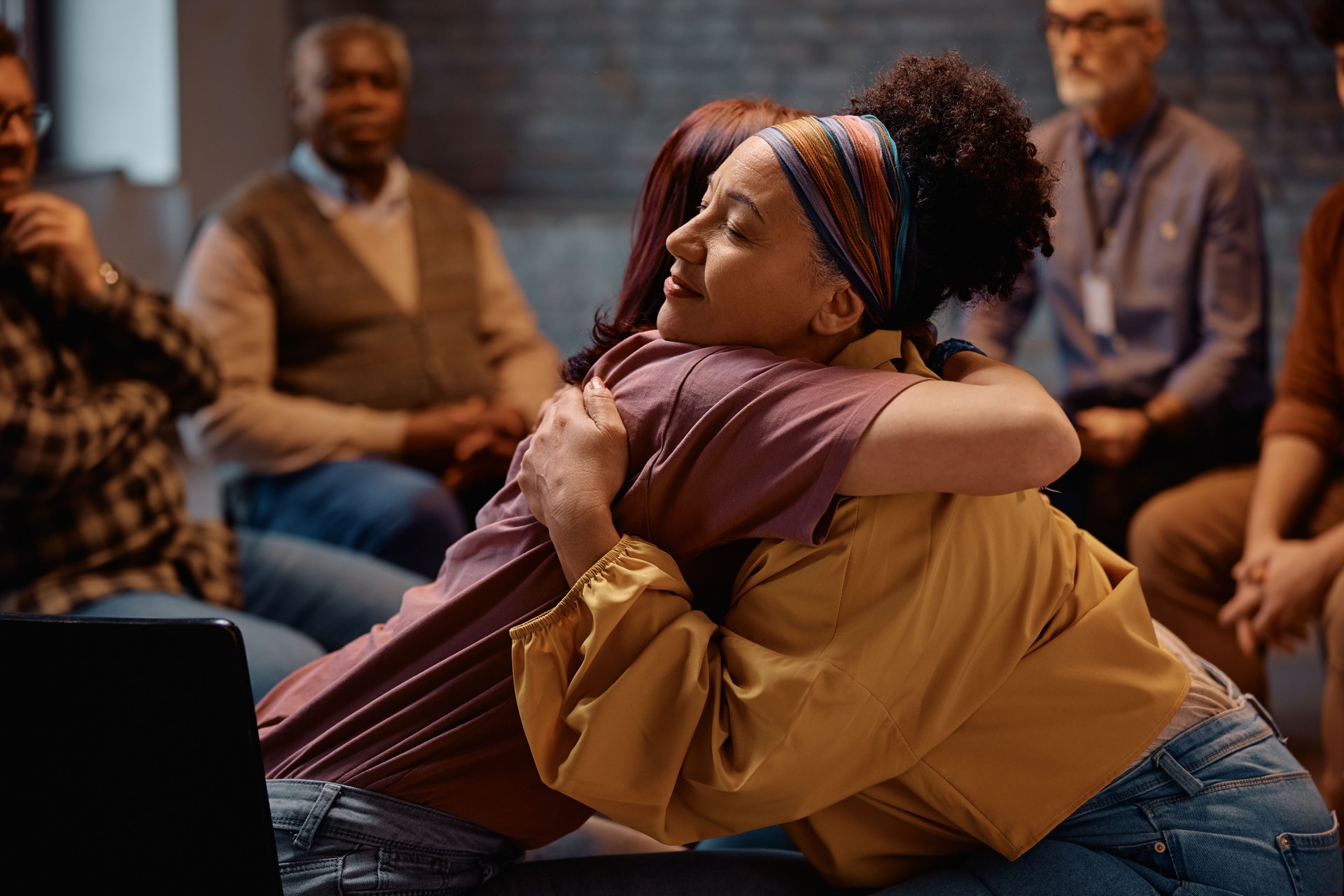 Supportive women embracing during group therapy at mental health center.